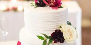 A white two-tier wedding cake decorated with pink and white flowers and a Mr & Mrs topper.