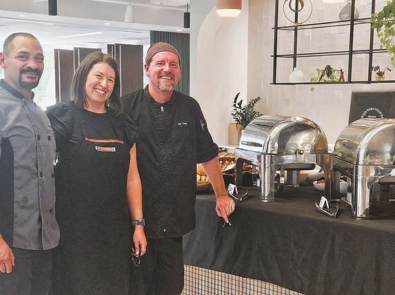 Three catering staff members standing in front of a buffet table with silver chafing dishes.