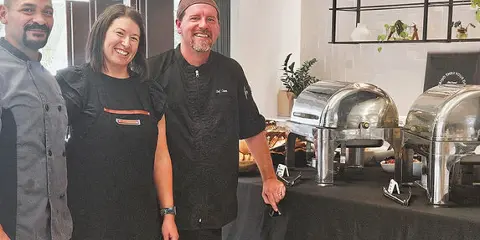 Three catering staff members standing in front of a buffet table with silver chafing dishes.
