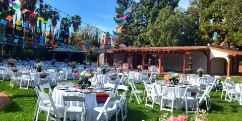 Outdoor wedding venue with set tables, white chairs, and a Spanish-style building under a blue sky.
