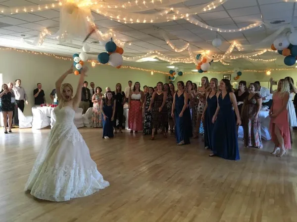 A bride dances on a wooden floor surrounded by wedding guests in a decorated reception hall.