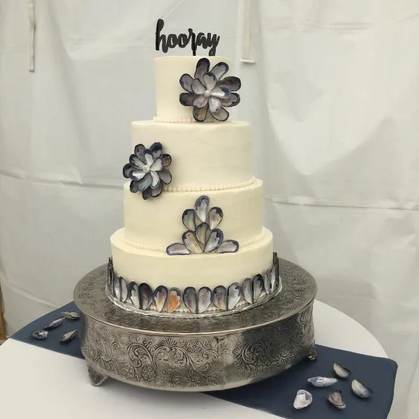 Four-tier white wedding cake decorated with blue and gray flowers on an ornate silver stand.