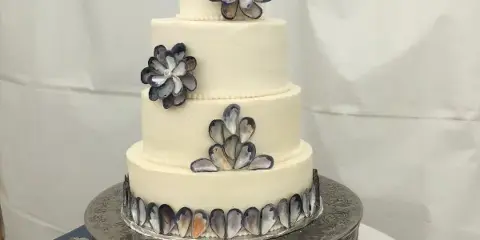 Four-tier white wedding cake decorated with blue and gray flowers on an ornate silver stand.