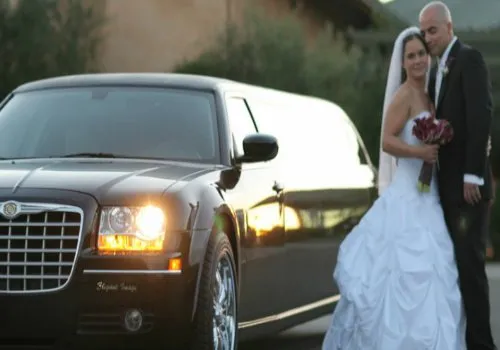 A bride and groom posing next to a black stretch limousine
