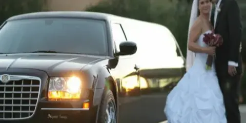 A bride and groom posing next to a black stretch limousine