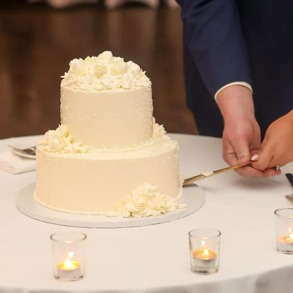 A two-tier white wedding cake with piped rosettes being cut by a couple at a table.