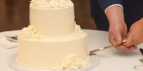 A two-tier white wedding cake with piped rosettes being cut by a couple at a table.