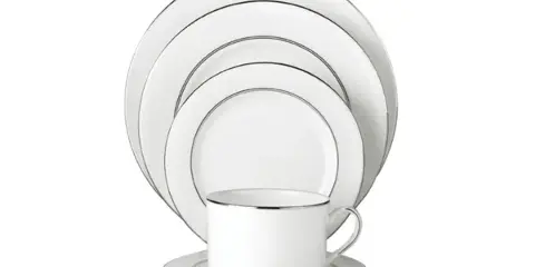 A set of white dinner plates and a matching cup with gold rims arranged on a white background.