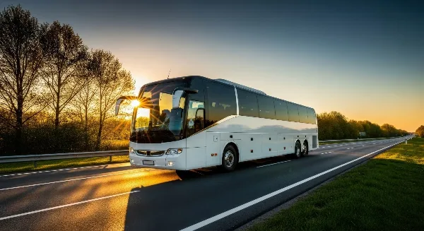 A white charter coach bus driving on a highway at sunset.