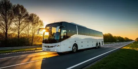 A white charter coach bus driving on a highway at sunset.