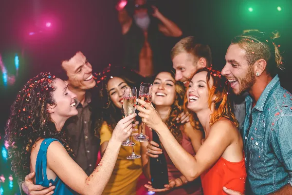 Group of smiling party guests toasting with champagne flutes under colorful event lighting.