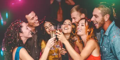 Group of smiling party guests toasting with champagne flutes under colorful event lighting.