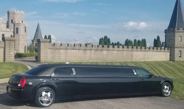 A black stretch limousine parked on a paved surface in front of a stone castle-like structure.