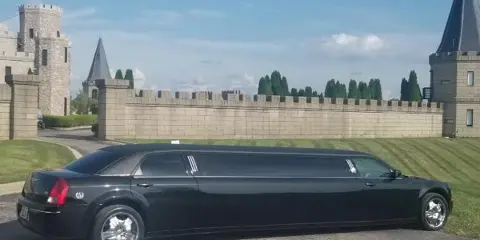 A black stretch limousine parked on a paved surface in front of a stone castle-like structure.