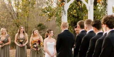A bride and groom standing at a floral-decorated arch during an outdoor wedding ceremony with their wedding party.