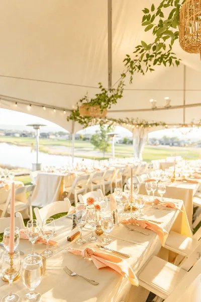 An outdoor wedding reception under a white tent with elegantly set tables, white chairs, and floral centerpieces.