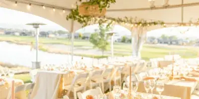 An outdoor wedding reception under a white tent with elegantly set tables, white chairs, and floral centerpieces.