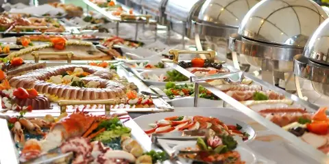 A catering buffet line featuring stainless steel chafing dishes and various prepared food platters.
