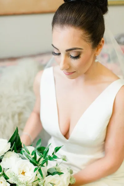 Bride with a sleek updo hairstyle and professional makeup holding a white bouquet