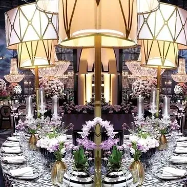 A formal event table setting featuring a large floral centerpiece, decorative lamps, and elegant place settings.