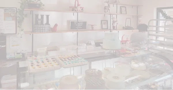 Bakery display case filled with cakes, cupcakes, and pastries with shelves of baked goods and decor in the background