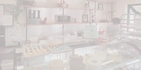 Bakery display case filled with cakes, cupcakes, and pastries with shelves of baked goods and decor in the background