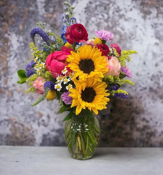 A colorful floral arrangement featuring sunflowers, roses, and other flowers in a glass vase.