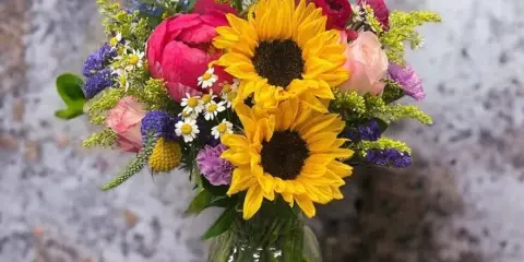 A colorful floral arrangement featuring sunflowers, roses, and other flowers in a glass vase.