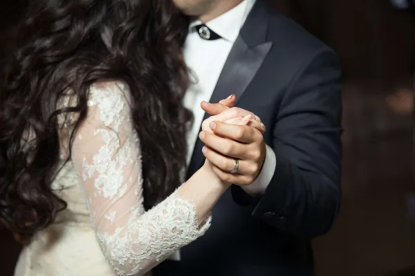 Close-up of a bride and groom holding hands, showing the bride's lace sleeve and the groom's suit.