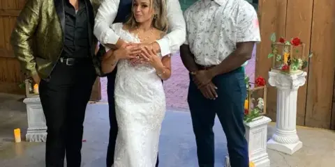 A wedding couple posing with two entertainment professionals at a rustic barn venue with a 'Happily Ever After' banner.