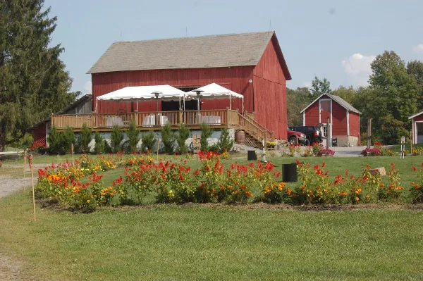 A red barn with a wooden deck and white event tents set in a rural field with flower beds.