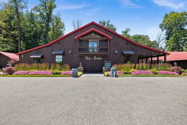 Exterior view of The Barn at Willow Lake Event Center, a large dark wooden building with a red roof and manicured landscaping.