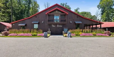 Exterior view of The Barn at Willow Lake Event Center, a large dark wooden building with a red roof and manicured landscaping.