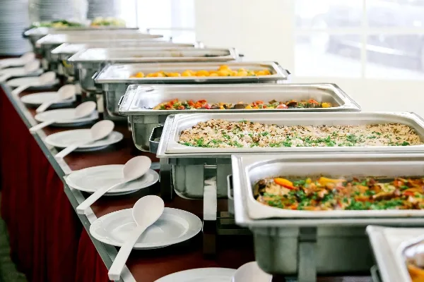 Buffet table with multiple chafing dishes of prepared food and serving plates