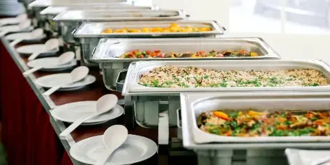 Buffet table with multiple chafing dishes of prepared food and serving plates