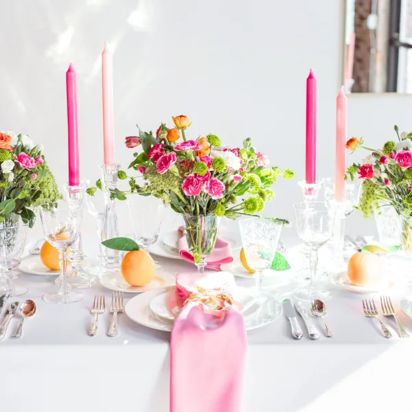 A professionally set event table featuring white plates, silver flatware, crystal glassware, pink napkins, and floral centerpieces.
