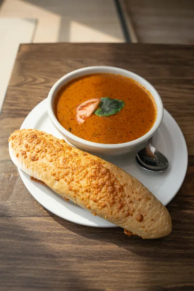 A bread roll and a bowl of tomato basil bisque served on a white plate.