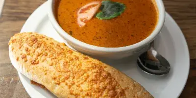 A bread roll and a bowl of tomato basil bisque served on a white plate.