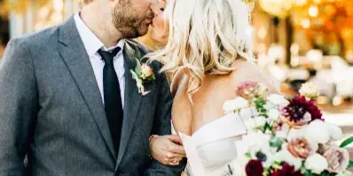 A bride and groom sharing a kiss outdoors with autumn foliage in the background.