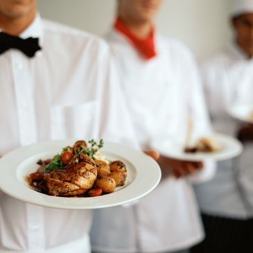 Catering servers in white uniforms holding plates of prepared food