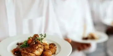 Catering servers in white uniforms holding plates of prepared food