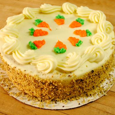 A round carrot cake with cream cheese frosting and decorative carrot-shaped icing on top.