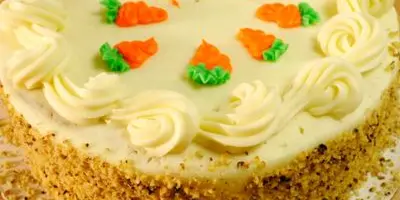 A round carrot cake with cream cheese frosting and decorative carrot-shaped icing on top.