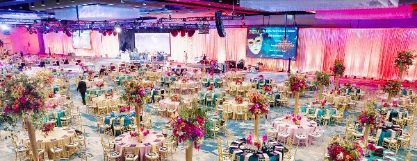 A large banquet hall filled with round tables, chairs, and floral centerpieces set up for a corporate event.