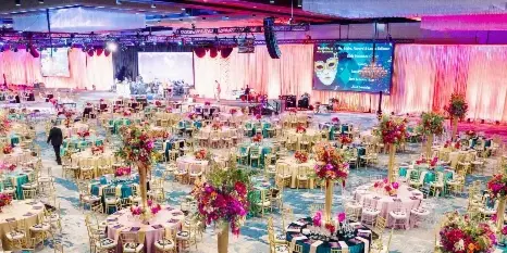 A large banquet hall filled with round tables, chairs, and floral centerpieces set up for a corporate event.