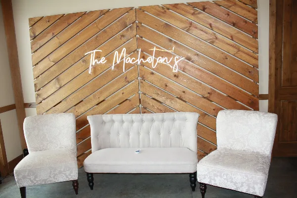 White upholstered sofa and chairs arranged in front of a wooden plank backdrop with a neon sign.