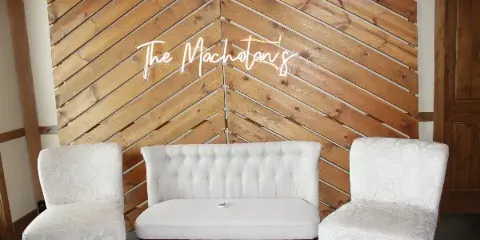 White upholstered sofa and chairs arranged in front of a wooden plank backdrop with a neon sign.