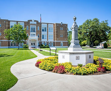 Exterior view of the Julien Poydras Museum and Arts Center building with a statue and landscaped grounds.