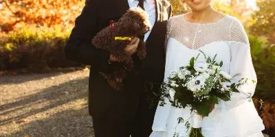 A wedding couple posing outdoors, with the bride holding a white and green floral bouquet.