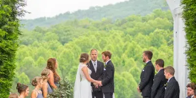 A bride and groom exchanging vows under a white arched trellis with a scenic mountain view in the background.